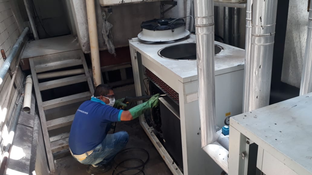 Imagem de homem limpando unidade condensadora de ar condicionado com lavadora de alta pressão